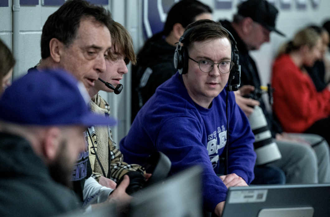 Alec Rome looks over to a screen while broadcasting a basketball game